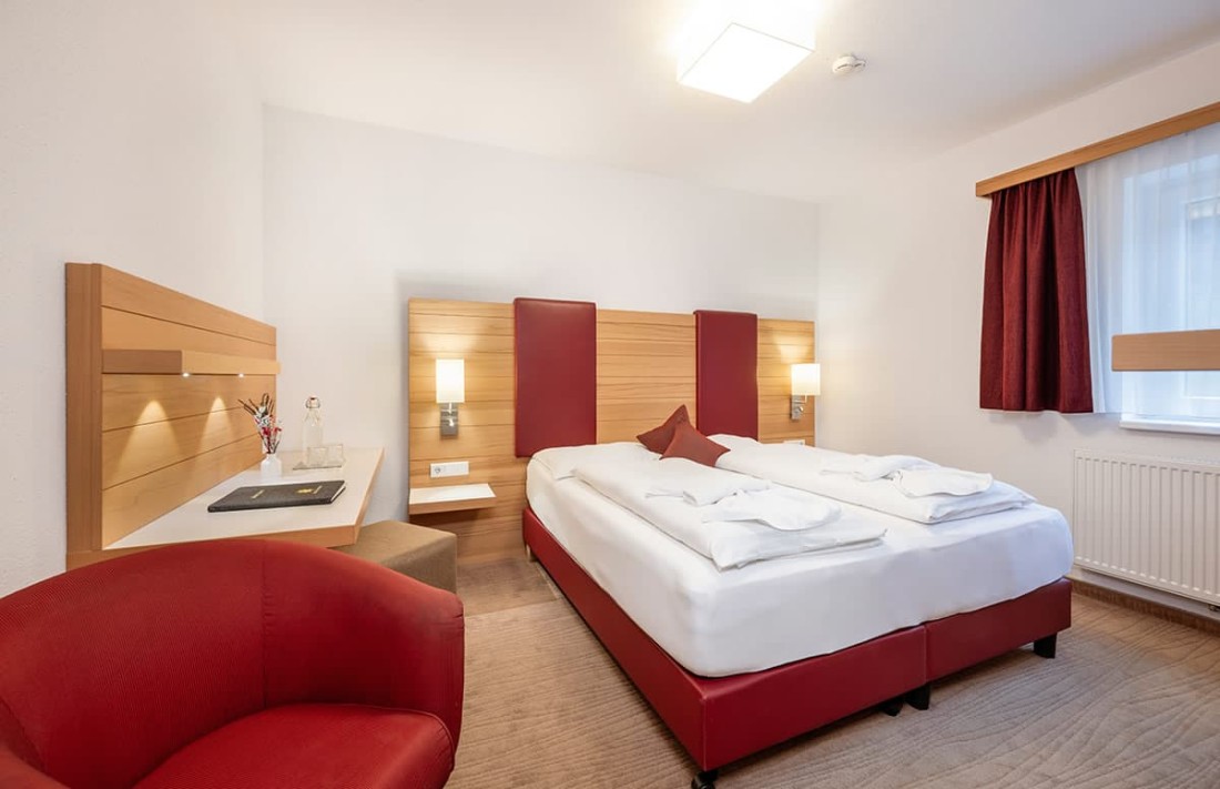 Modernes Doppelzimmer mit Doppelbett, rotem Sessel und Schreibtisch