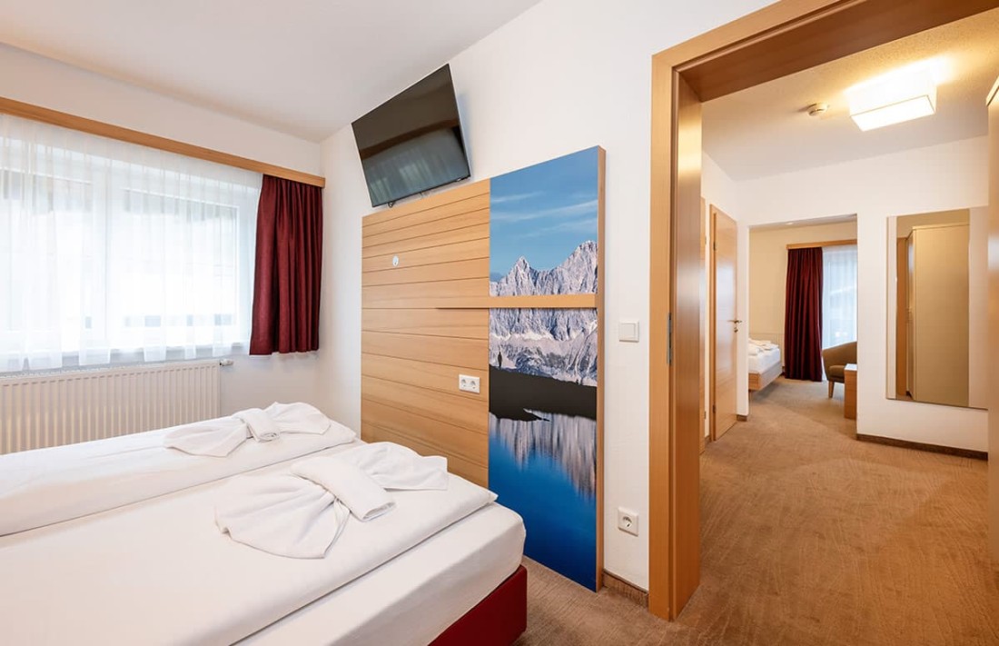 Helles Familienzimmer mit zwei Betten, TV und Bergbild an der Wand