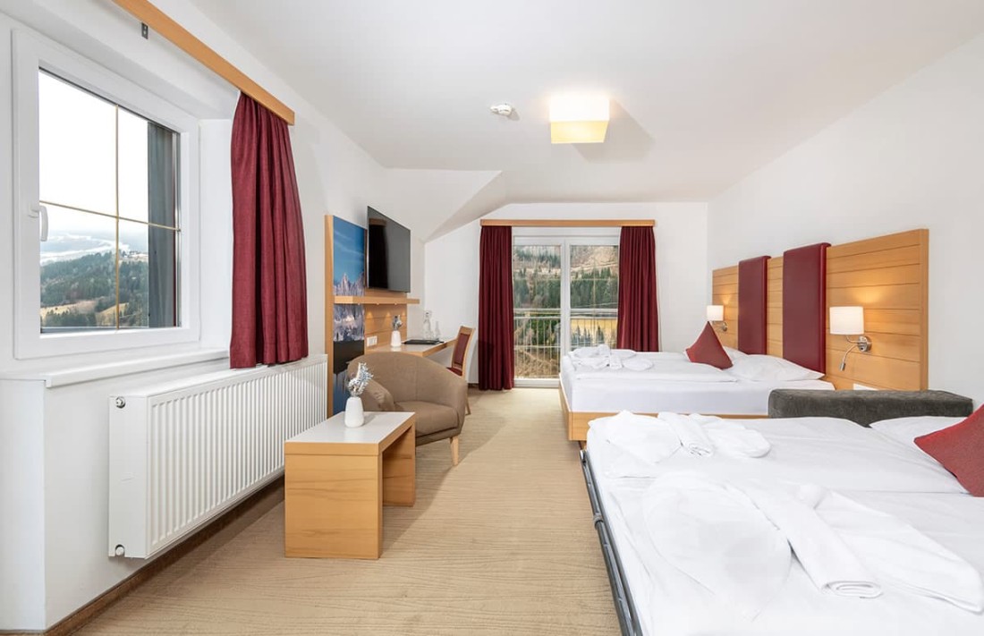 Helles Familienzimmer Standard mit zwei Betten, roten Vorh&auml;ngen und Blick auf eine bergige Landschaft