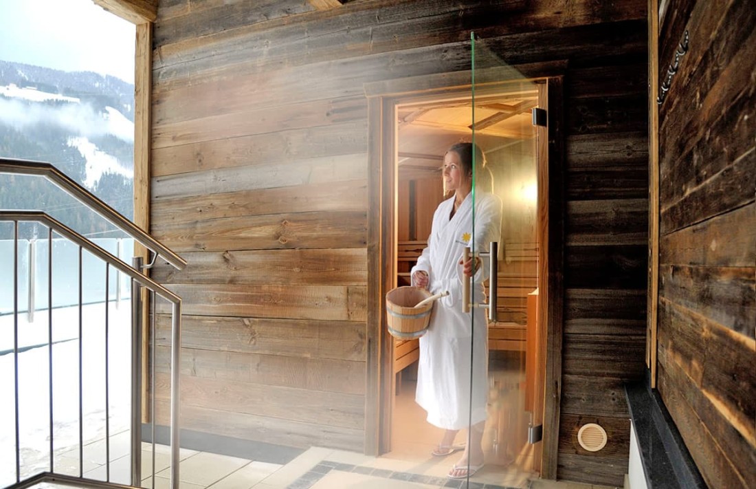 Person im Bademantel verl&auml;sst eine Sauna mit Holzw&auml;nden