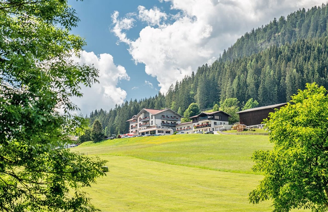 Hotle Sonnschupfer in Schladming inmitten gr&uuml;ner Landschaft und umgeben von dichten W&auml;ldern unter blauem Himmel
