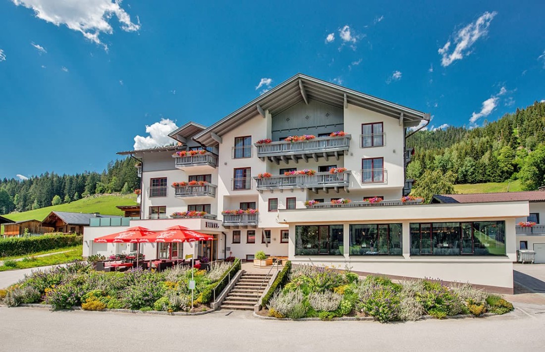 Hotel Sonnschupfer in Schladmking mit Balkonen und roten Blumenk&auml;sten vor H&uuml;geln und blauem Himmel
