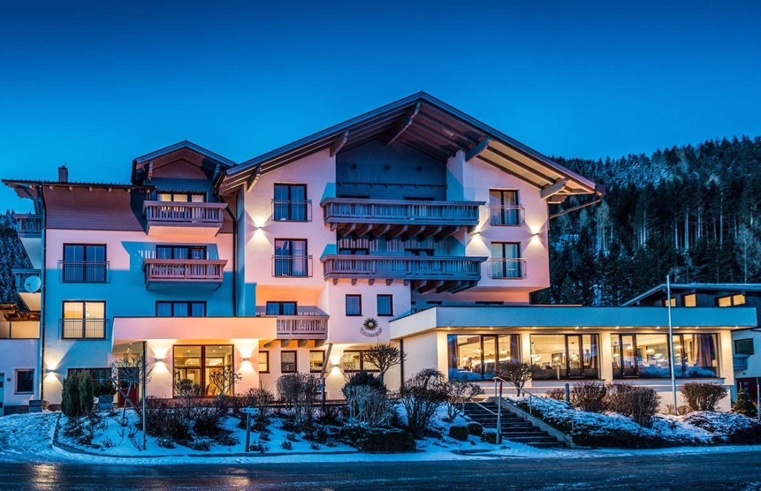 Beleuchtetes Hotel Sonnschupfer vor einem schneebedeckten Wald bei D&auml;mmerung
