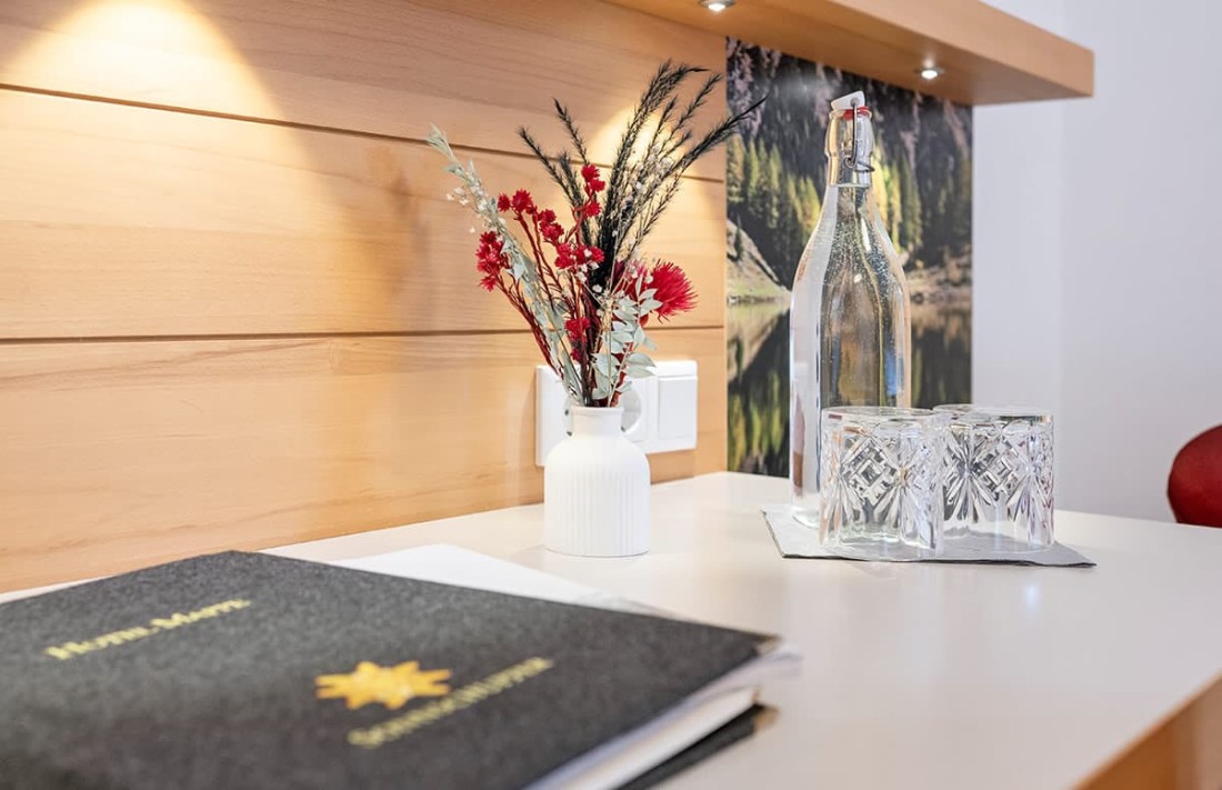 Vase mit roten Blumen und Gl&auml;sern auf einem Tisch mit Holzverkleidung und Leuchte