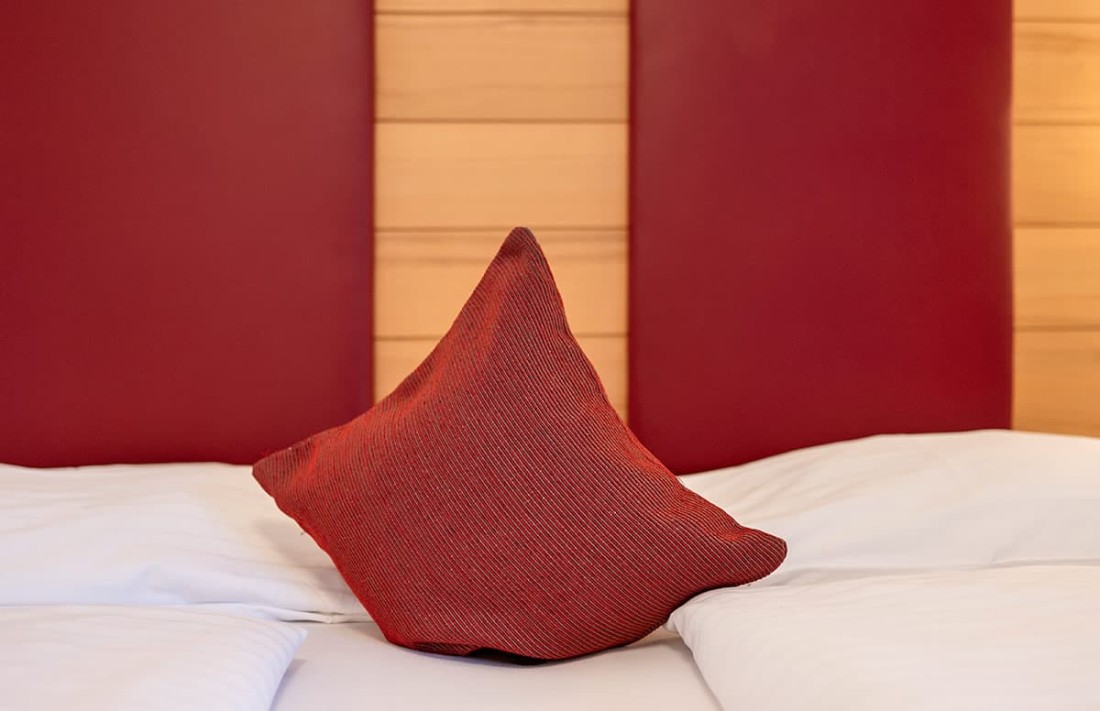 Ein rotes Kissen liegt auf einem Bett mit roten Kopfteilpolstern