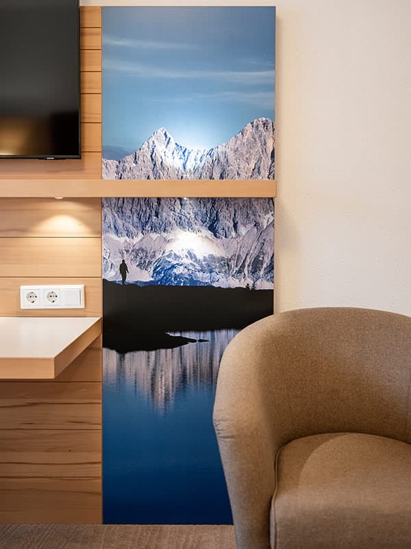 Zimmerdetail mit gem&uuml;tlichem Sessel und Wandbild vom Spiegelsee in der Region Schladming-Dachstein